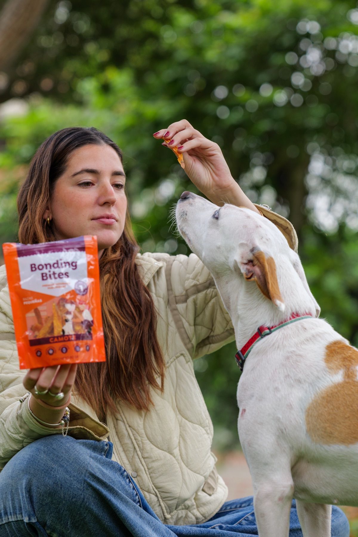 Una chica le da un premio a su perro mientras sostiene una bolsa de Bonding Bites